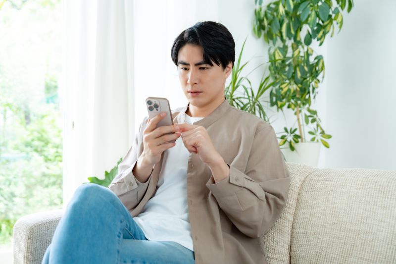 自宅でスマホを見る男性(イメージ写真)